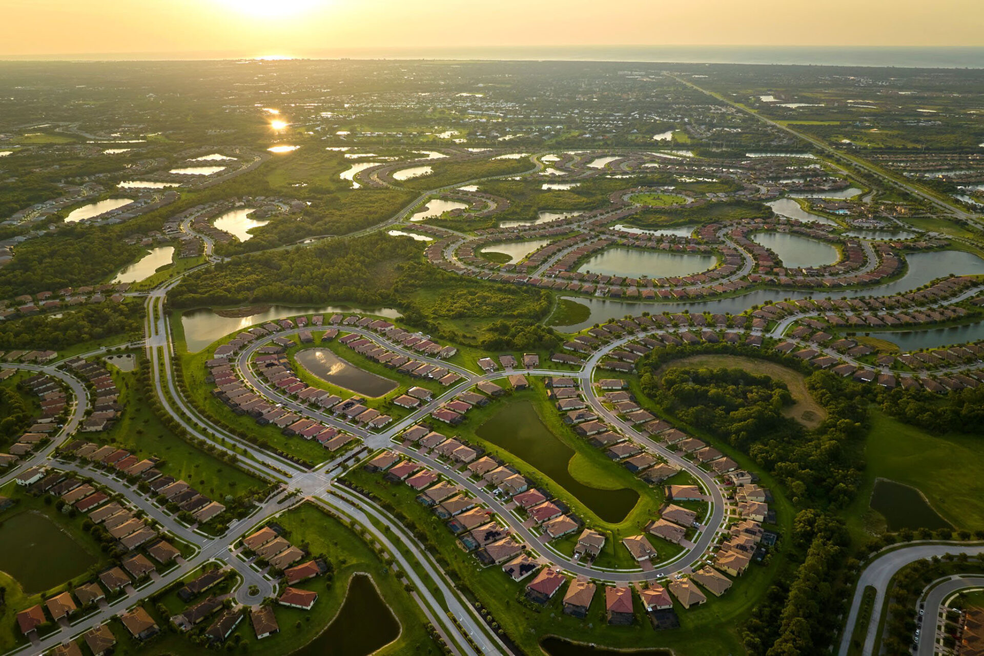 Aerial view of tightly packed homes in Florida closed living clubs with lake water in the middle. Family houses as example of real estate development in american suburbs.